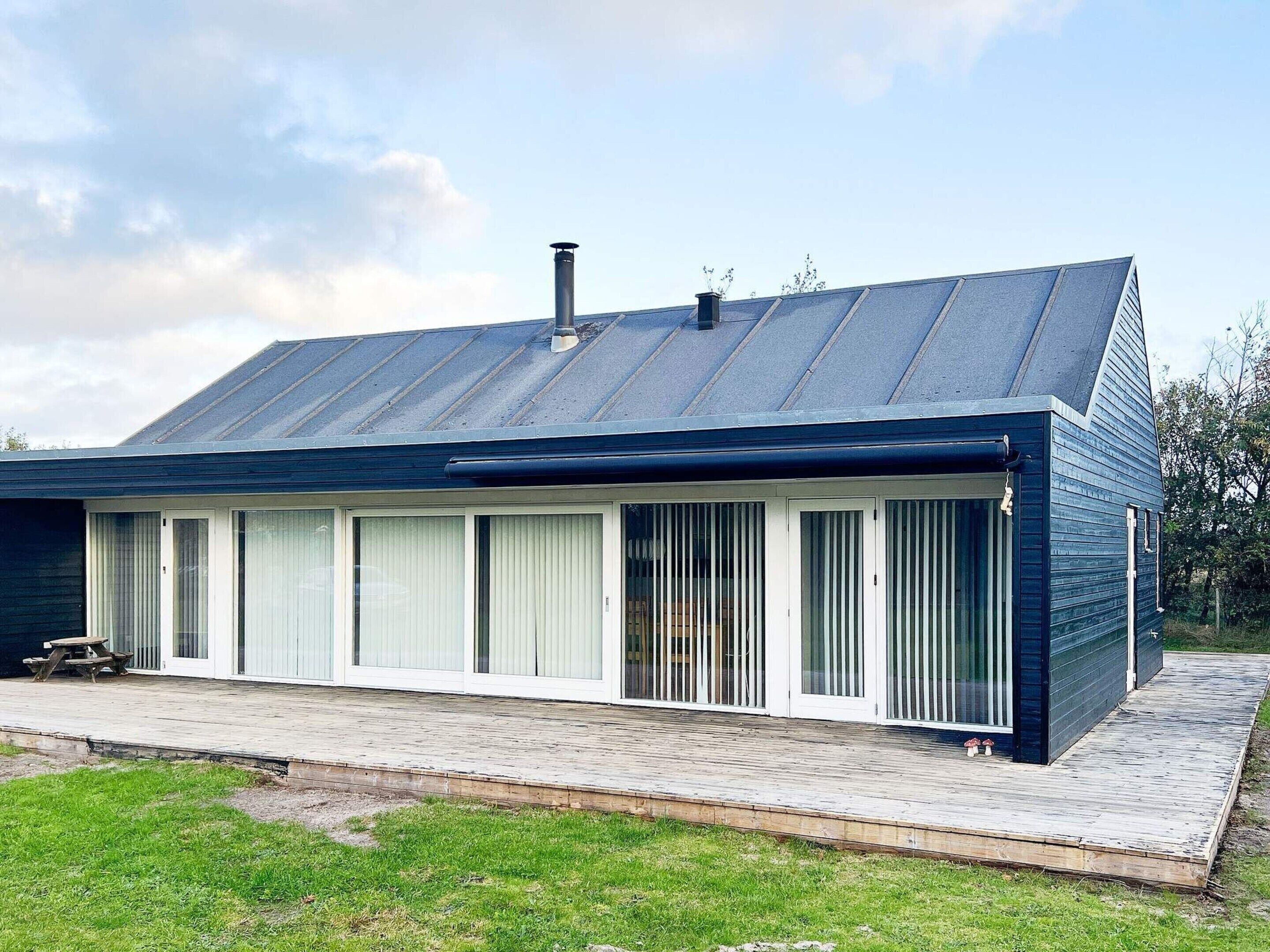 A modern house with a metal roof, large windows, and a wooden deck.