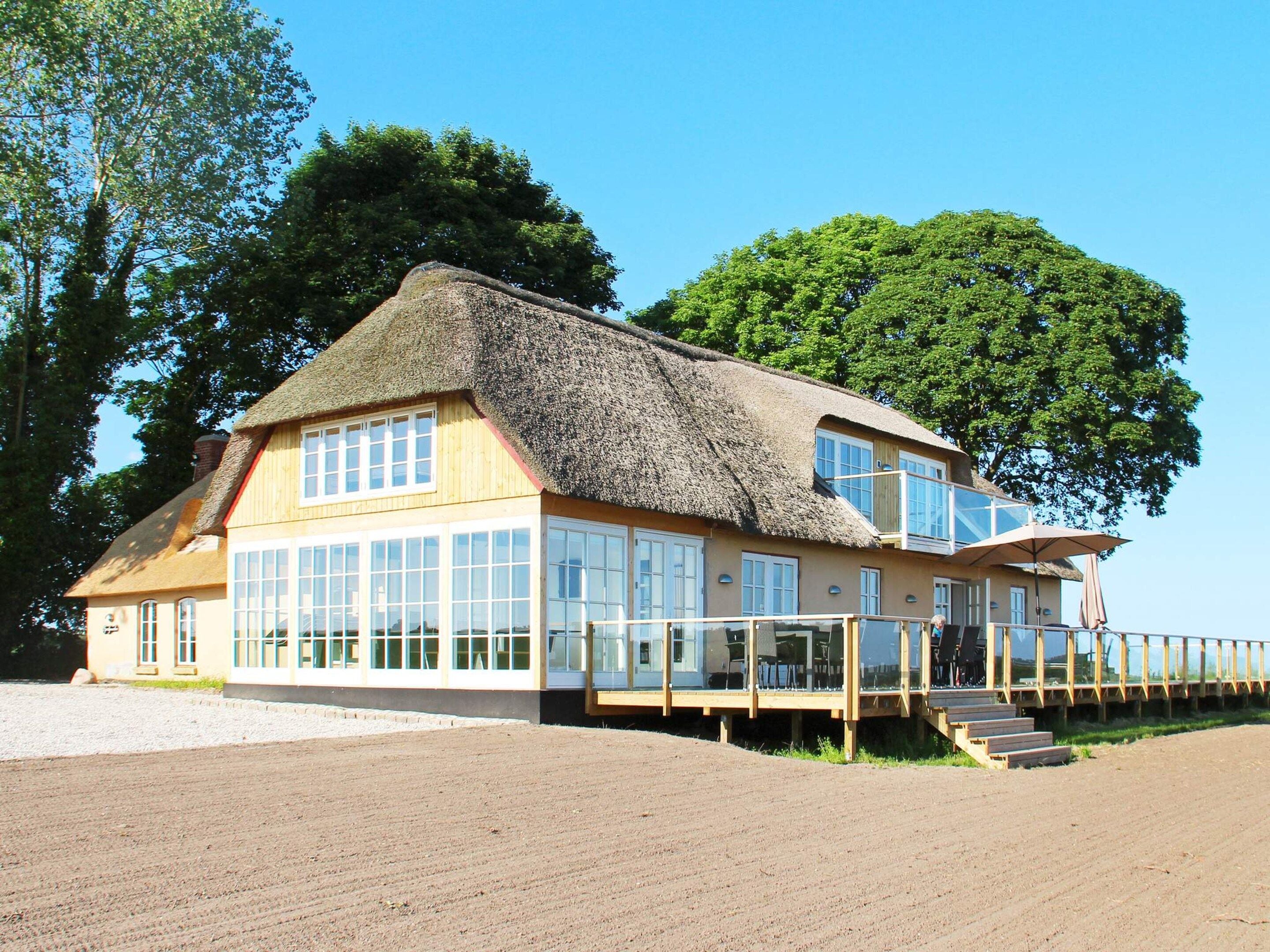 Et hus med stråtækt tag, store vinduer og en træterrasse.