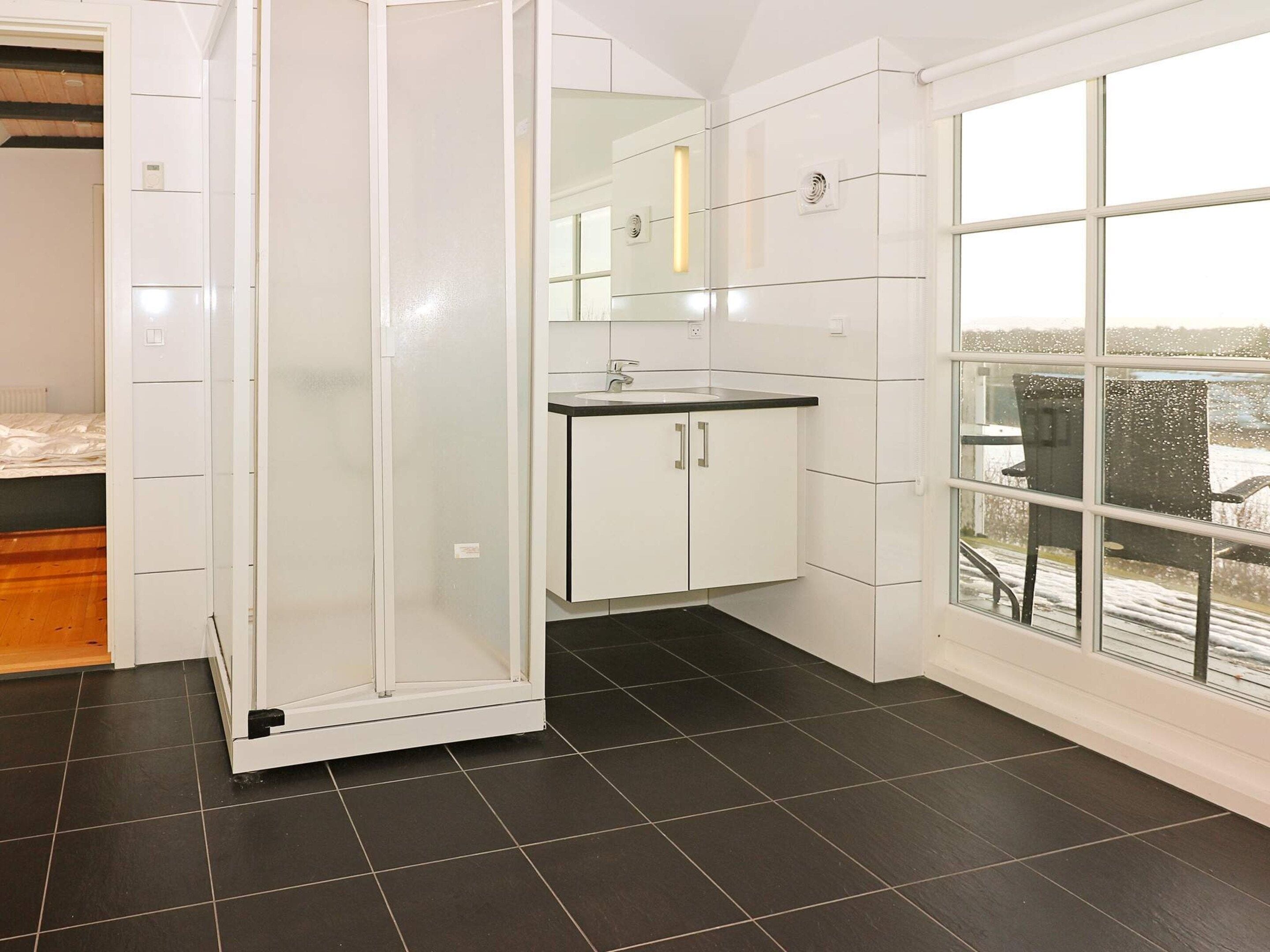 A modern bathroom with a glass shower enclosure, a white sink, and a large window offering a view of the outdoors.