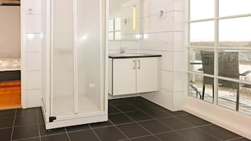 A modern bathroom with a glass shower enclosure, a white sink, and a large window offering a view of the outdoors.