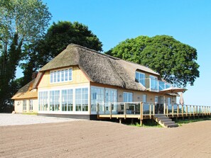 A thatched-roof house with large windows and a wooden deck. - 14 Person Holiday Home in Havndal (Havndal)
