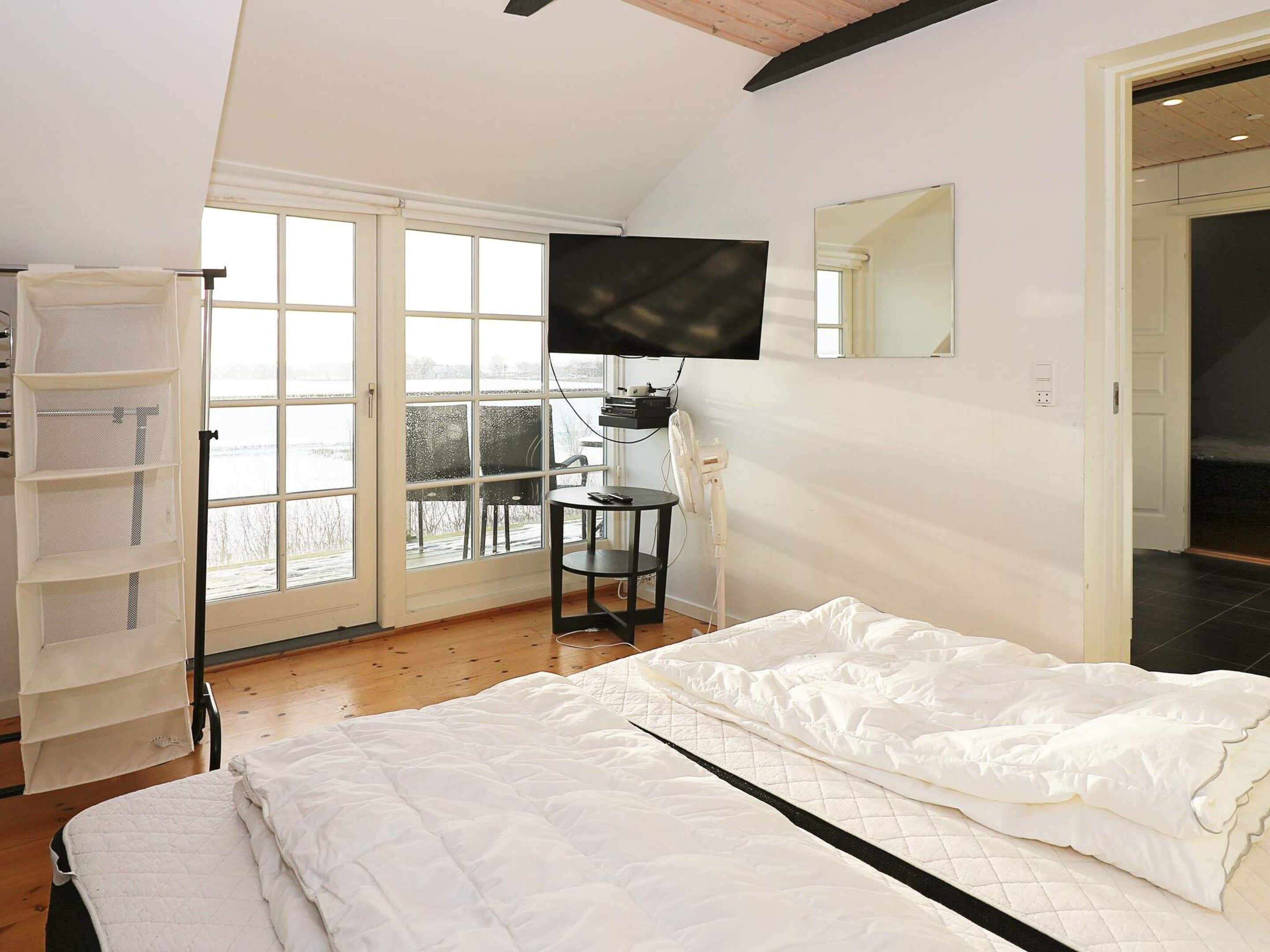Un dormitorio con cama, escritorio, silla, televisor y ventana con vistas a un paisaje nevado.