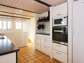 A kitchen with white cabinets, a black countertop, a microwave, and an oven. - 14 Person Holiday Home in Havndal (Havndal)