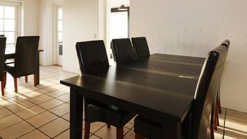 A dining area with a long table and chairs, white brick walls, and tiled flooring.