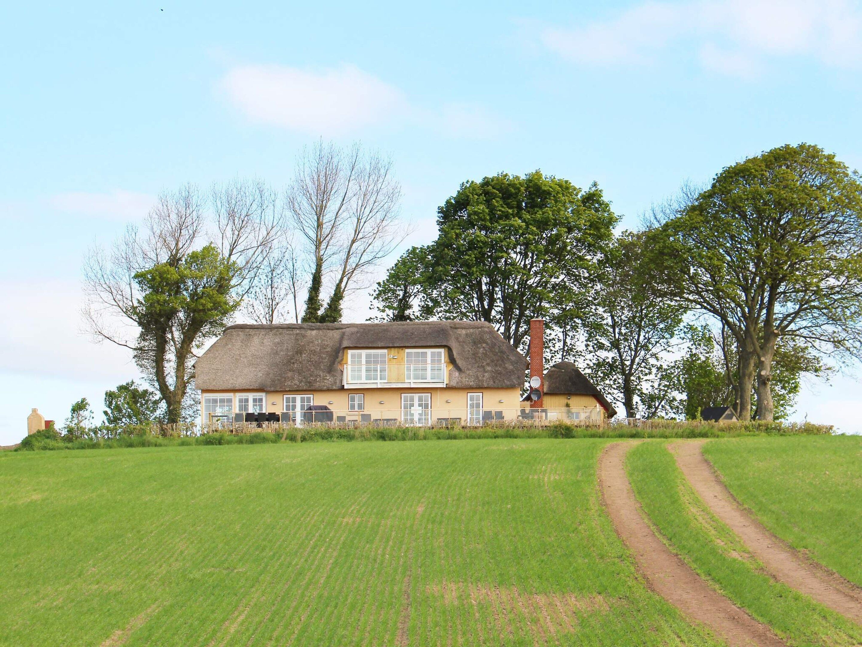 A thatched-roof house with a large lawn and a dirt path leading to it.