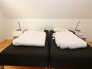 A double bed with a black mattress and white bedding, flanked by white nightstands with lamps. - 14 Person Holiday Home in Havndal (Havndal)