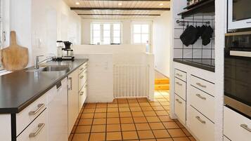 Una cocina con gabinetes blancos, encimera negra, piso de baldosas y ventana con vistas.