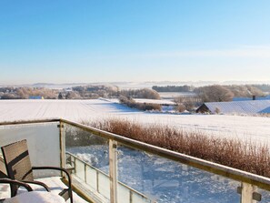 A snow-covered landscape with a clear sky, a wooden deck, and a view of distant fields and buildings. - 14 Person Holiday Home in Havndal (Havndal)