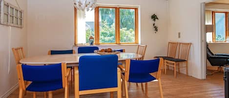 A dining area with a wooden table and blue chairs, a hanging light fixture, and a window with a view of greenery.