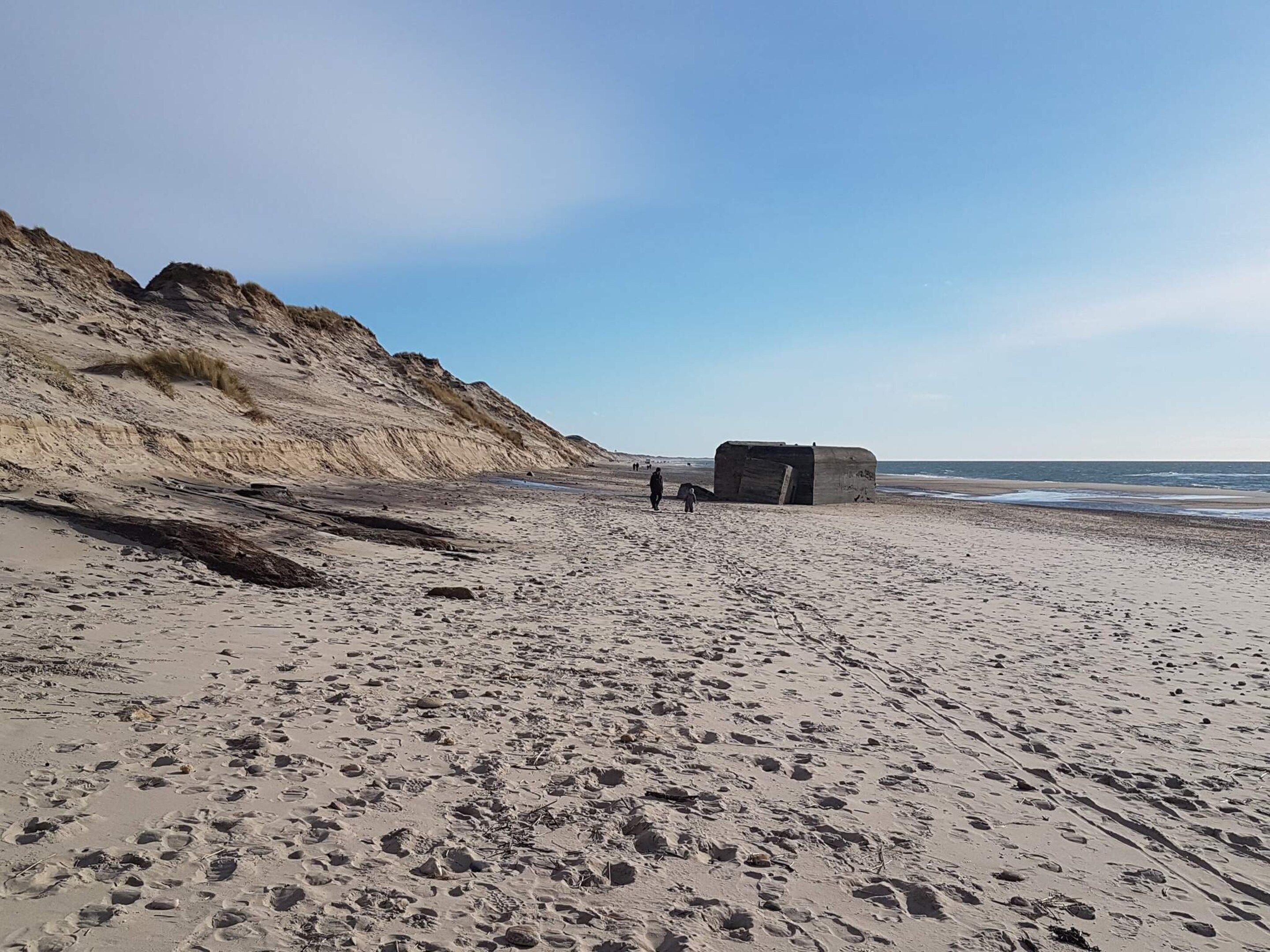 A sandy beach with footprints, a large rock formation, and a small structure.