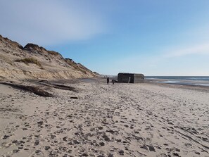 A sandy beach with footprints, a large rock formation, and a small structure. - 10 Person Holiday Home in Ulfborg (Ulfborg)