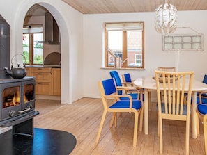A modern kitchen with a wood-burning stove, a dining area with blue chairs, and a large window with a view of a brick building.