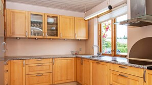 Cozinha com armários de madeira, pia de aço inoxidável e janela com vista para área verde.