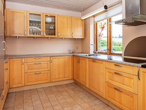 Cozinha com armários de madeira, pia de aço inoxidável e janela com vista para área verde.