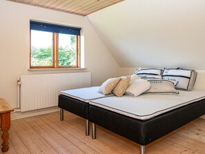 A bedroom with a bed, pillows, a window with a view of greenery, a radiator, and a wooden floor.