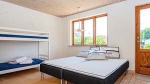 Quarto com beliche, uma cama de solteiro com travesseiros, janela com vista e porta de madeira.