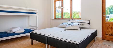 A room with a bunk bed, a single bed with pillows, a window with a view, and a wooden door.