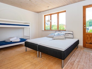 Quarto com beliche, uma cama de solteiro com travesseiros, janela com vista e porta de madeira.