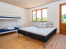 A room with a bunk bed, a single bed with pillows, a window with a view, and a wooden door.