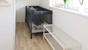 A room with a crib, a white bench, a window with a view, and a shelf with items. - 8 Person Holiday Home in Hadsund (Hadsund)