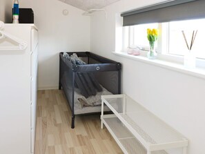 A room with a crib, a white bench, a window with a view, and a shelf with items. - 8 Person Holiday Home in Hadsund (Hadsund)