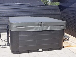 A large, dark-colored outdoor storage unit with a lid, positioned on a paved surface with a wooden deck in the background. - 8 Person Holiday Home in Hadsund (Hadsund)