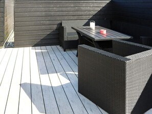 An outdoor patio with a table and chairs, a small white object on the table, and a dark-colored wall in the background. - 8 Person Holiday Home in Hadsund (Hadsund)