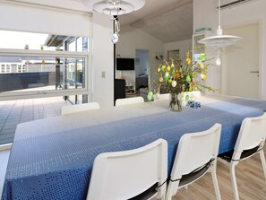 A modern dining area with a large table, white chairs, and a vase with flowers.