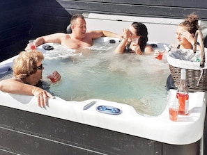 Un groupe de personnes dans un jacuzzi équipé d’un panneau de commande numérique, entouré d’un panier en osier et de bouteilles.