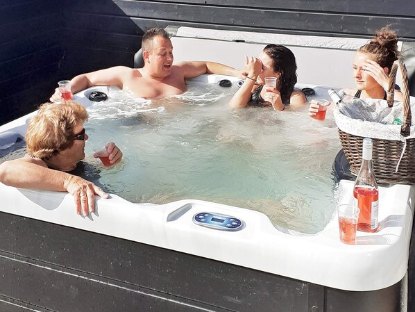 A group of people in a hot tub with a digital control panel, surrounded by a wicker basket and bottles.