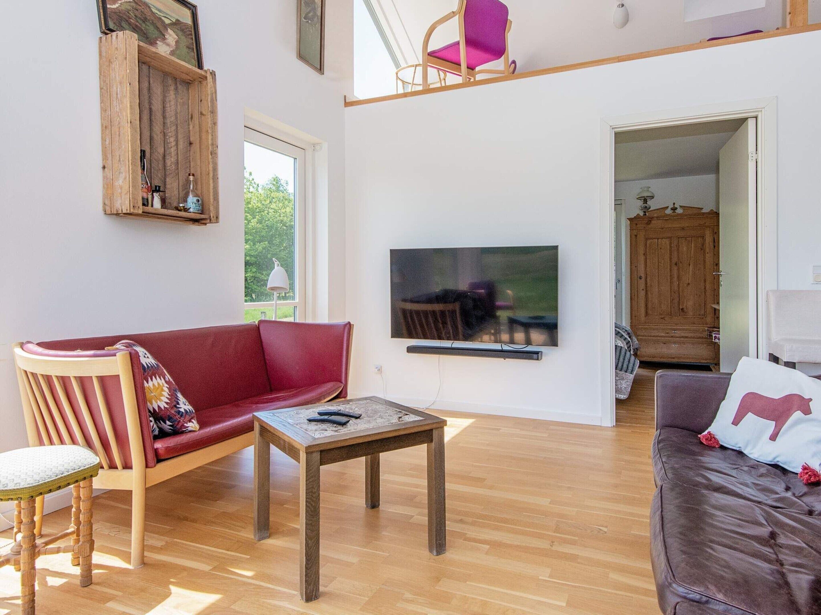 Un salon avec un canapé rouge, une table basse en bois et un téléviseur fixé au mur.