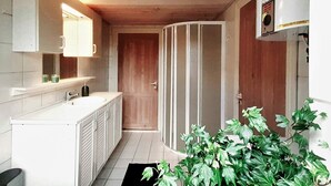 Une salle de bain moderne avec un plafond en bois, des meubles blancs, un grand miroir et une plante en pot.