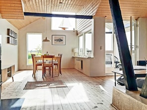 A spacious room with a high ceiling, wooden beams, a dining area with a table and chairs, a window with a view of greenery, and a large mirror. - 8 Person Holiday Home in Lokken-by Traum (Lokken)