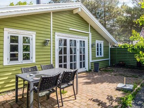 Uma casa verde com um pátio que inclui uma mesa, cadeiras, uma janela e um pequeno jardim.