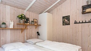 A bedroom with two beds, wooden walls, a white wardrobe, and shelves with plants and pictures.