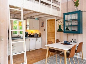 Une cuisine compacte avec des meubles blancs, une table à manger avec des chaises et un meuble vert avec des portes en verre.