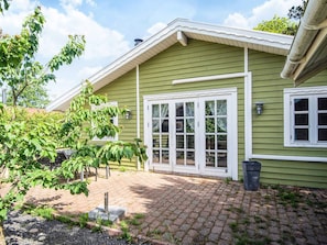 A green house with a brick patio, white trim, and a large front window. - 4 Person Holiday Home in Hemmet (Hemmet)