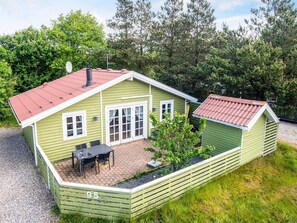 En grön trästuga med ett rött tak, en uteplats med ett bord och stolar samt ett litet förråd.