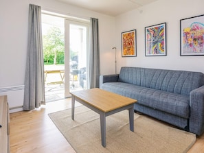 A modern living room with a grey sofa, a wooden coffee table, and a large window with curtains.