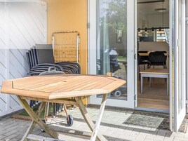 Una mesa de madera con ruedas, una silla y un vidrio que da a una habitación con una mesa y sillas.