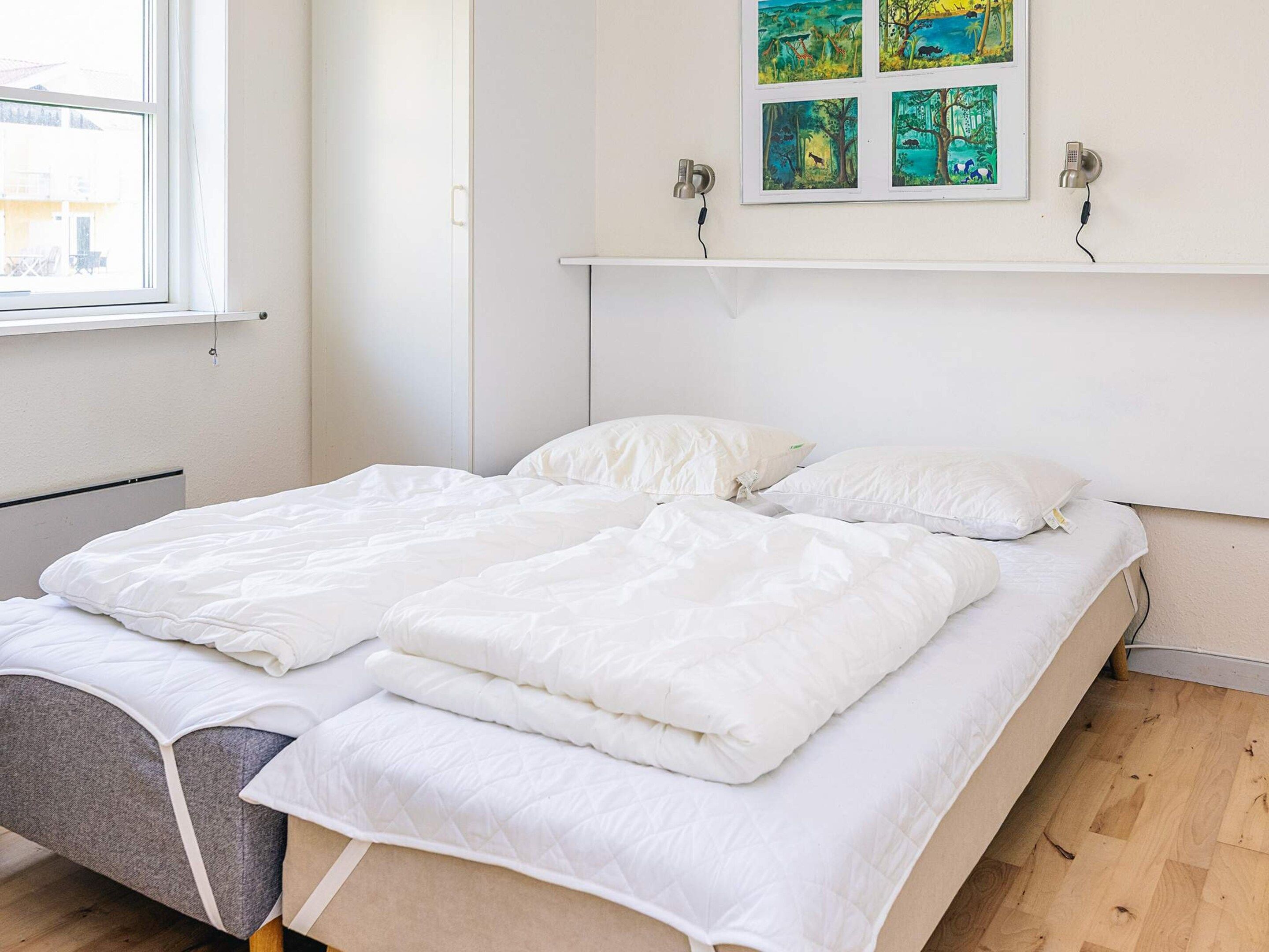 A neatly made bed with white bedding in a room with a window, a wall-mounted shelf, and a framed picture above the bed.