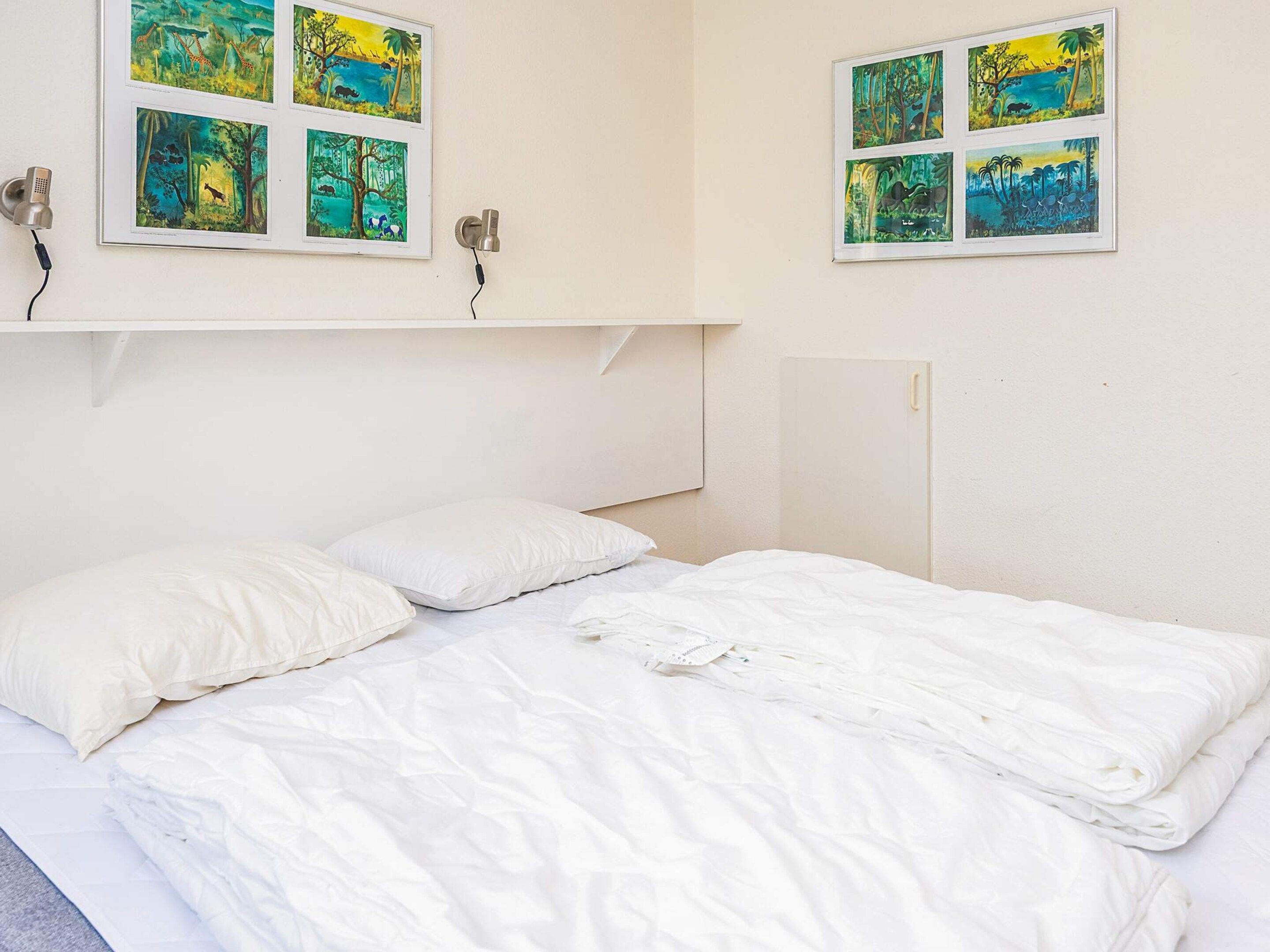 Ein Bett mit weißer Bettwäsche, eine weiße Wand und ein Regal mit gerahmten Bildern.
