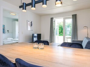 A modern room with a wooden dining table, two chairs, a sofa, a TV, and a large window with curtains. - 4 Person Holiday Home in Hals (Hals)