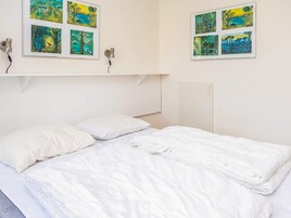 Una habitación con una cama, dos almohadas y una estantería con marcos.