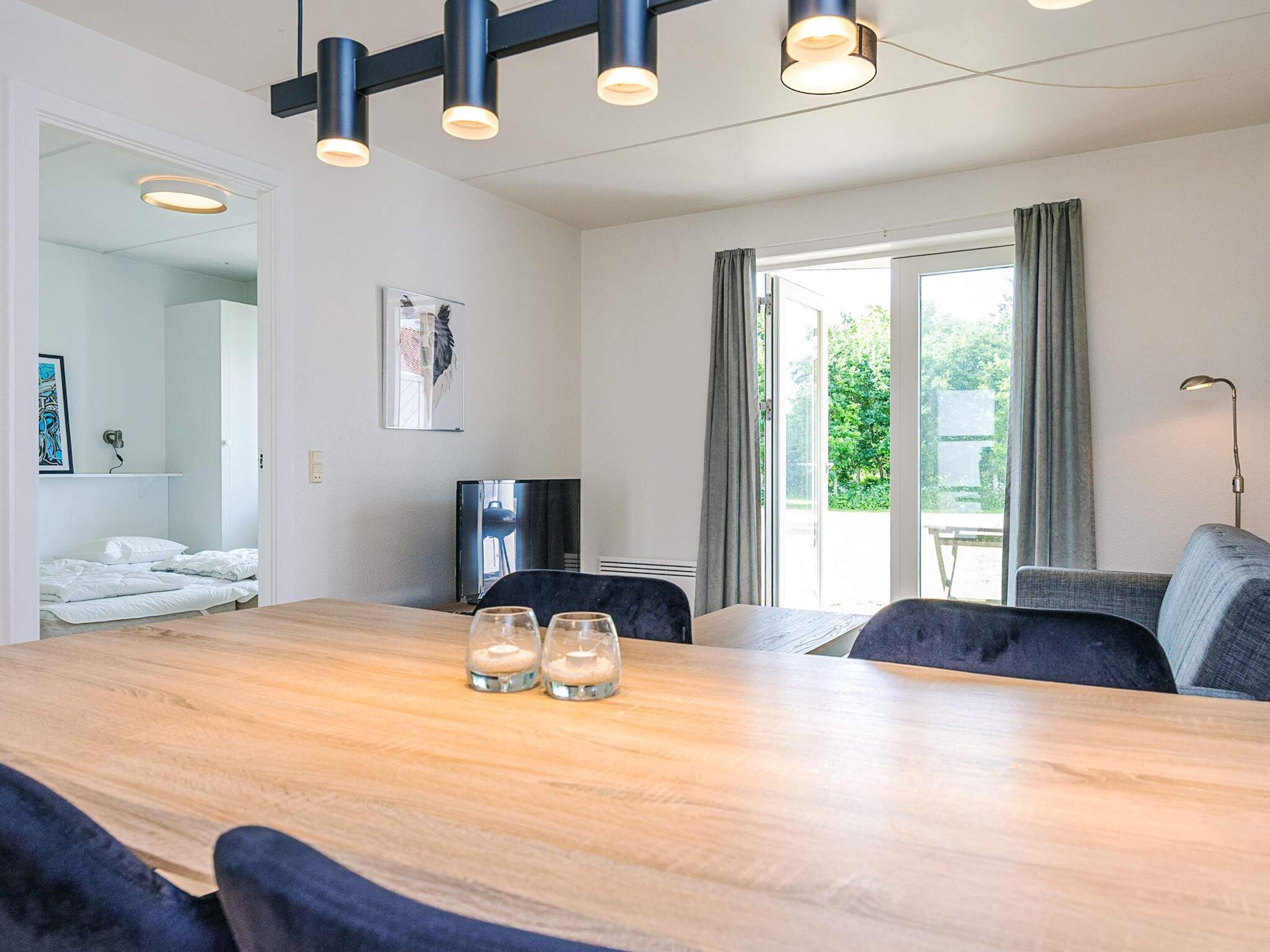 Una habitación moderna con una mesa de comedor de madera, dos sillas, un sofá, un televisor y una ventana con cortinas.