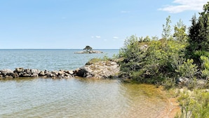 Kystlandskab med klart vand, en klippefyldt kystlinje og frodig vegetation.