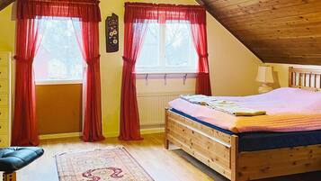 A bedroom with a wooden bed, red curtains, a bedside lamp, and a patterned rug.