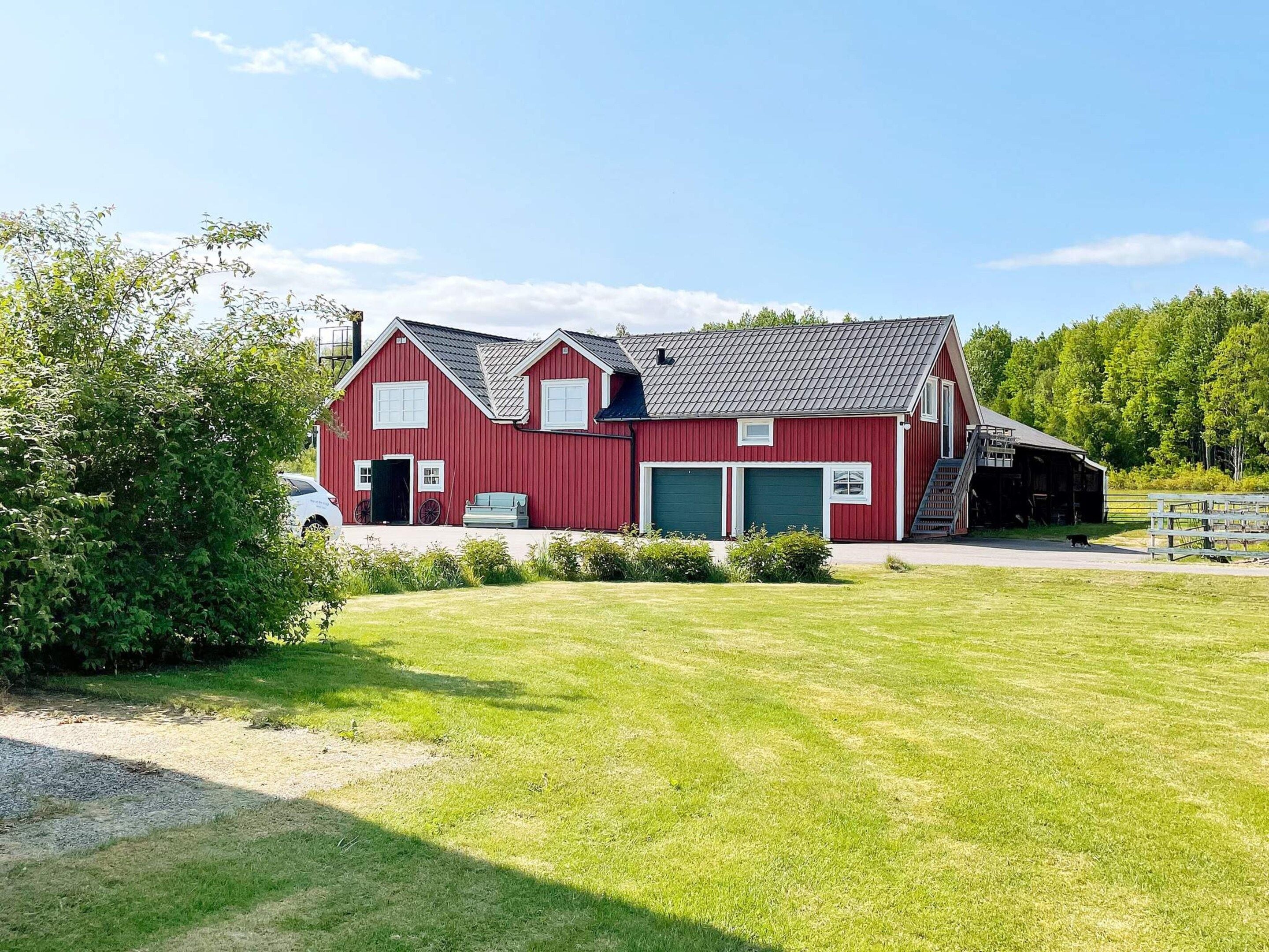 A red barn with a green garage door, a covered porch, and a dirt path leading to it.
