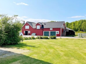 A red barn with a green garage door, a covered porch, and a dirt path leading to it. - 8 Person Holiday Home in Bralanda (Bralanda)
