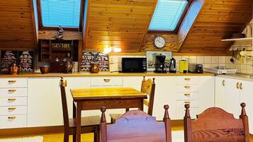 A kitchen with wooden cabinets, a dining table, chairs, a clock, and a window with blinds.
